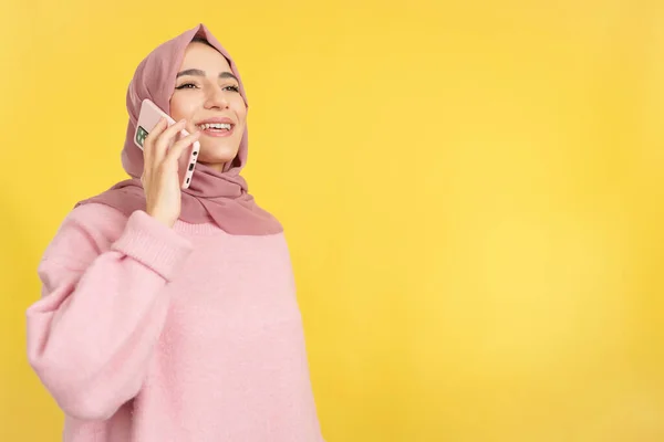 黄色の背景を持つスタジオで携帯電話と話す幸せなイスラム教徒の女性 — ストック写真