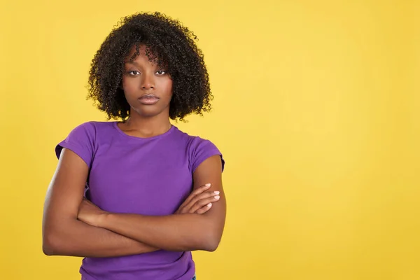 Angry woman with afro hair posing with arms crossed in studio with yellow background