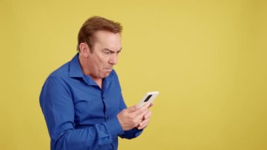 Stüdyoda sarı arka planda cep telefonuna bakan yetişkin bir adam için sürpriz oldu.