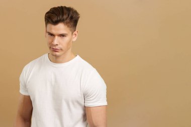 Baştan çıkarıcı bir adam stüdyoda kahverengi arka planla dikilirken kameraya bakıyor.