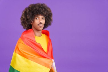 Stüdyoda lgbt bayrağıyla sarılı kameraya gülümseyen ciddi bir Afrikalı adam.