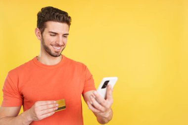 Beyaz adam sarı arka planlı online alışveriş yapmak için cep telefonu ve kartını kullanıyor.