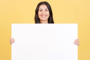 Stüdyoda sarı arka planda kameraya gülümseyen bir kadın boş bir paneli tutuyor.