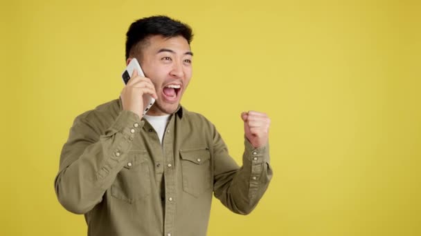 Emocionado Hombre Chino Celebrando Mientras Utiliza Teléfono Móvil Estudio Con — Vídeos de Stock