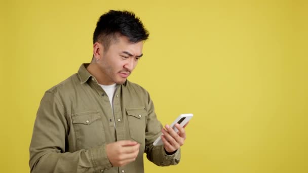 黄色の背景を持つスタジオでモバイルを使用している間に心配してジェスチャー中国人男性 — ストック動画