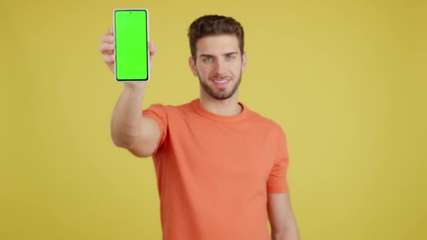 一个有着黄色背景的高加索人在工作室里拿着手机的绿色屏幕 — 图库视频影像