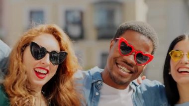 Sokakta kalp şeklinde güneş gözlüğü takıp gülen çok ırklı bir arkadaş grubunun yavaş çekim videosu.