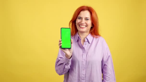 Студийное Видео Жёлтым Фоном Зрелой Женщины Показывающее Хроматический Экран Мобильного — стоковое видео
