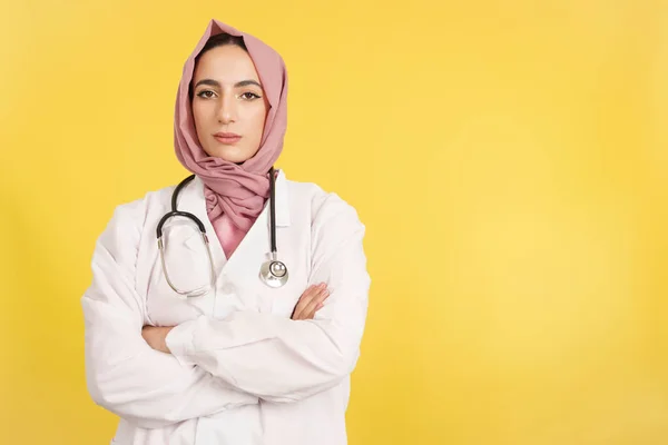 深刻な女性イスラム教徒医師とともに腕交差見ますカメラでスタジオで黄色の背景 — ストック写真