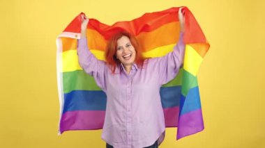 Lgbt gökkuşağı bayrağıyla sarılı mutlu, kızıl saçlı, olgun bir kadın.