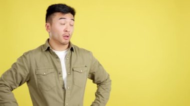 Amazed chinese man pointing surprised to the side in studio with yellow background