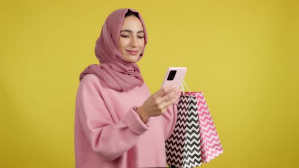 穆斯林妇女在整理购物袋时使用手机 黄色背景 — 图库视频影像