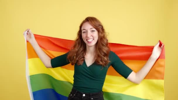 Ευτυχισμένη Κοκκινομάλλα Γυναίκα Τυλιγμένη Σημαία Lgbt Στο Στούντιο Κίτρινο Φόντο — Αρχείο Βίντεο