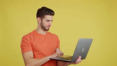 Stüdyoda sarı arka planda dizüstü bilgisayara bakarken beyaz bir adam kutlama yapıyor.