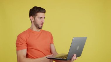 Caucasian man with a surprised look using a laptop in studio with yellow background