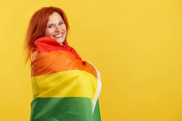 Szczęśliwa Ruda Dojrzała Kobieta Owinięta Tęczową Flagą Lgbt Studio Żółtym — Zdjęcie stockowe