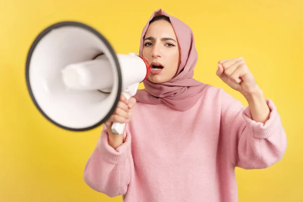 怒り狂ったイスラム教徒の女性は黄色の背景を持つスタジオでスピーカーを使用して叫んで — ストック写真