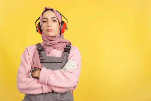黄色の背景を持つスタジオでカメラを見て仕事の制服で深刻なイスラム教徒の女性大工 — ストック写真