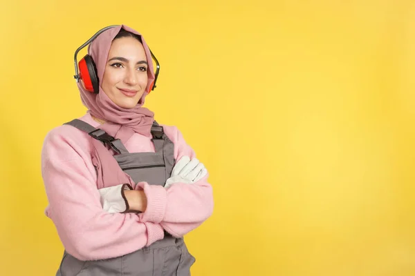黄色の背景を持つスタジオで交差腕を離れて立っているイスラム教徒の女性大工 — ストック写真