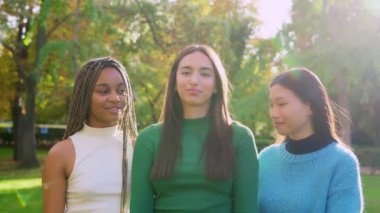 Parkta kucaklaşan ve gülümseyen üç mutlu çoklu etnik arkadaşın yavaş çekim videosu.