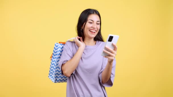 ショッピングバッグを持ちながら携帯電話を使っている幸せな白人女性 ミッドショット — ストック動画