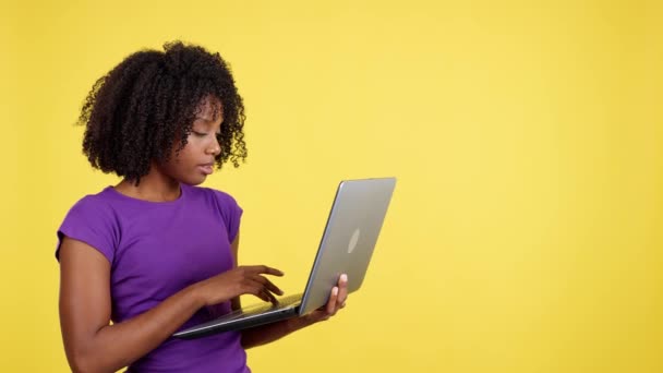 在有黄色背景的工作室里 非洲裔妇女看上去像一台带着震惊表情的笔记本电脑 — 图库视频影像