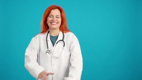 在蓝色背景的工作室里微笑着站着的红头发女医生 — 图库视频影像