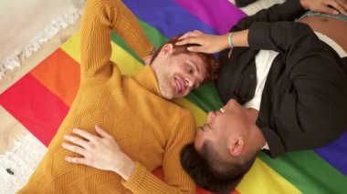Bir lgbt bayrağının üzerinde yatarken gülümseyen mutlu bir çiftin yavaş çekim videosu.