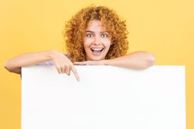Sarı arka planlı, kıvırcık saçlı ve boş bir paneli gösteren bir stüdyo resmi.