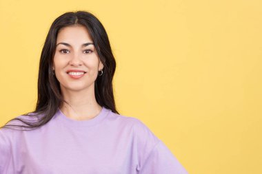 Mutlu kadın kameraya bakıyor. Stüdyoda rahat ve sarı arka planda.