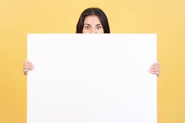 Stüdyoda sarı arka planı olan boş bir panelin arkasında saklanan sürpriz bir kadın.