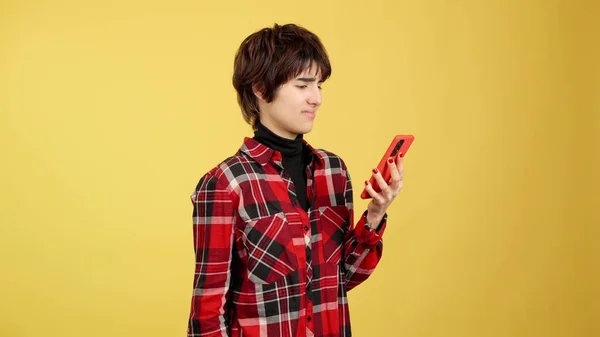 Angry androgynous person using a mobile phone in studio with yellow background