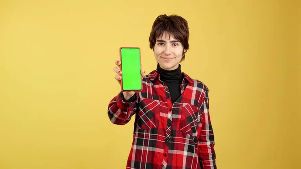 Androgynous person showing a chroma mobile screen in studio with yellow background