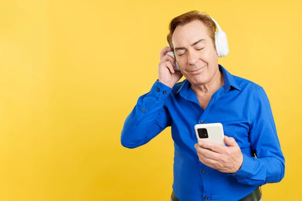 Relaxed Mature Man Listening Music Headphones Mobile Phone Studio Yellow — Stock Photo, Image
