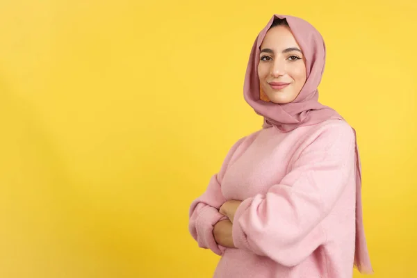 腕を組んで立っているイスラム教徒の女性は黄色の背景を持つスタジオでカメラを見て渡り — ストック写真