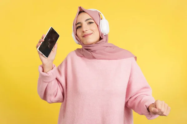 Счастливая Мусульманка Танцует Слушает Музыку Мобильном Телефоне Студии Желтым Фоном — стоковое фото