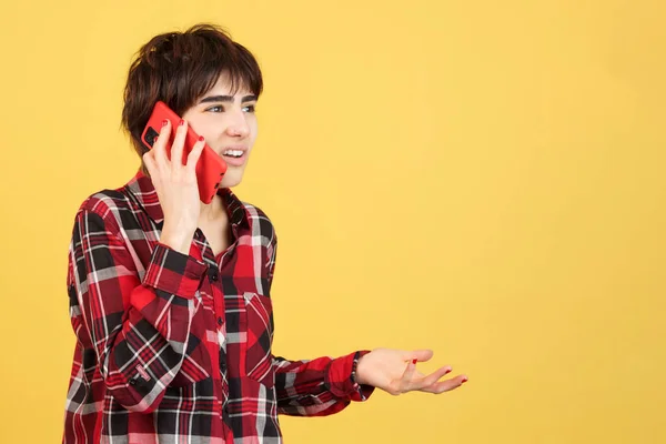Angry androgynous person talking to the mobile in studio with yellow background