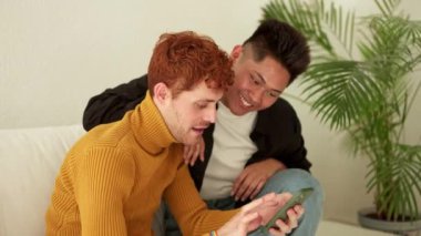 Evde cep telefonu kullanan çok ırklı mutlu bir eşcinsel çiftin yavaş çekim videosu.
