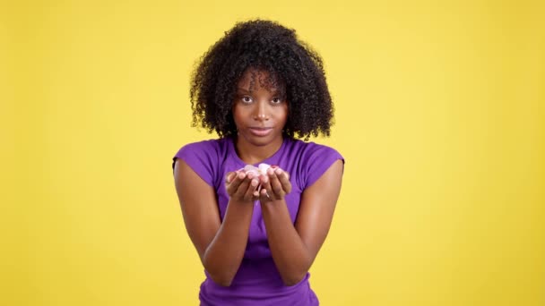 Iloinen Afro Nainen Puhaltaa Konfetteja Juhliessaan Studiossa Keltaisella Taustalla — kuvapankkivideo