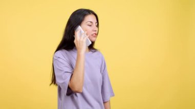 Angry caucasian woman talking to the mobile in studio with yellow background