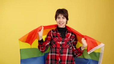 Stüdyoda sarı arka planda bir lgbt bayrağıyla sarılı Androgynous kişi