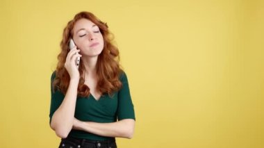 Stüdyoda sarı arka planda cep telefonuyla konuşan kızgın kızıl saçlı kadın.
