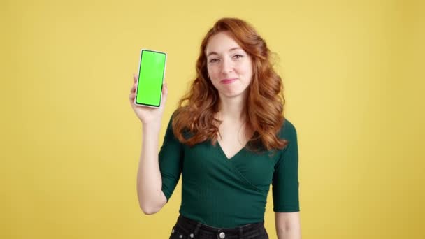 Рудоволоса Щаслива Жінка Представляє Мобільний Телефон Хромовим Екраном Студії Жовтим — стокове відео