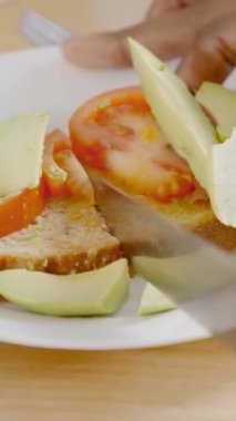 Yavaş çekim. Avokado ve domatesli sağlıklı bir tost kesen birinin yakın çekim videosu.