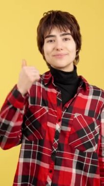 Androgynous person gesturing approval with the thumb up in studio with yellow background