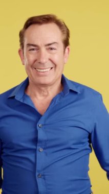 Happy mature man gesturing agreement raising a thumb up in studio with yellow background