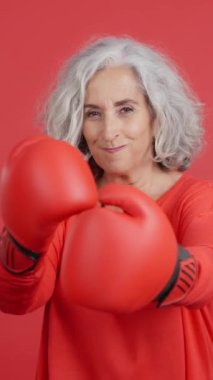 Studio video with red background of a mature woman in fighting pose wearing boxing gloves