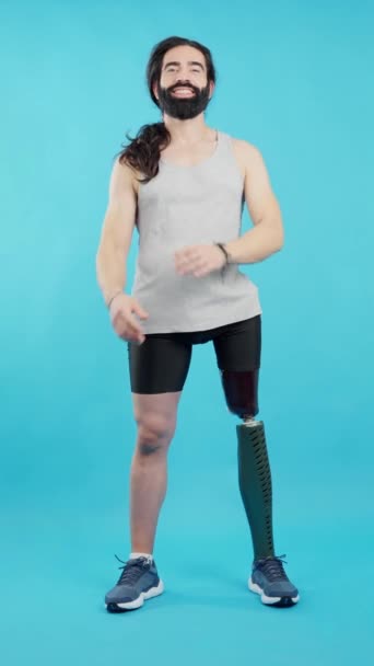 彼の足の上に義肢を持つ立っている白人のスポーツマンの青の背景を持つスタジオビデオ — ストック動画