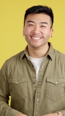 Chinese man laughing and looking at camera in studio with yellow background