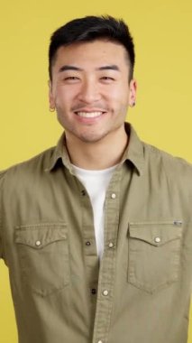 Happy chinese man gesturing agreement raising a thumb up in studio with yellow background